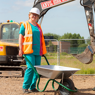 PDSA vet holding a wheelbarrow with green handles on a dig site