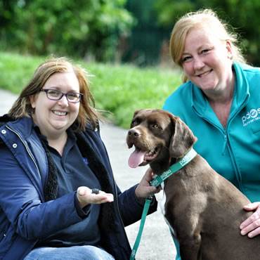 Milton, a brown Springer Spaniel crossbreed, sits next to his owner, Janice Latreche, and PDSA Vet Nurse Kylie Jones who taught the First Aid course that saved Milton's life.