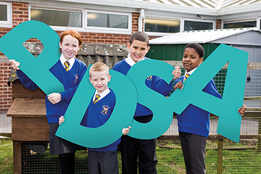 A photo of four schoolchildren, each holding a large letter, spelling out PDSA
